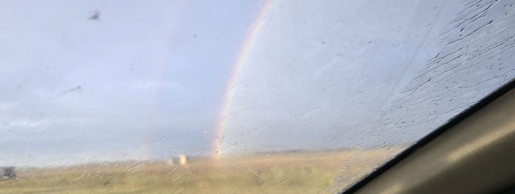 A rainbow spans across an Alberta prairie field as viewed from an Alberta highway.