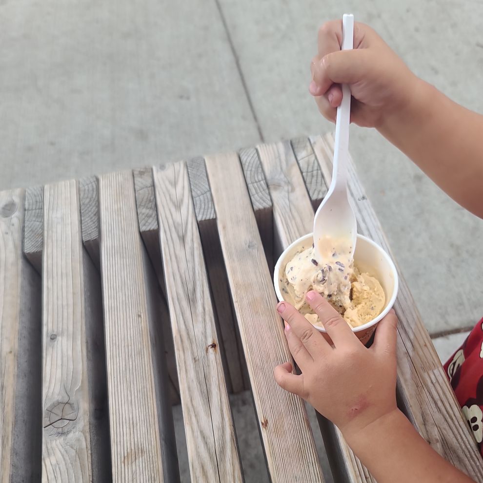 A cup of Kind ice cream held by a toddler on a sunny day - 1 scoop salted caramel, 1 scoop mint chip