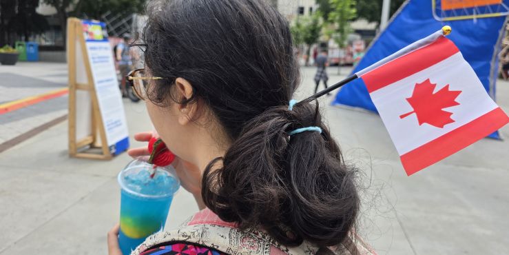A 3/4 upper profile view from the rear of a lovely young person with a Canada flag placed in their hair.