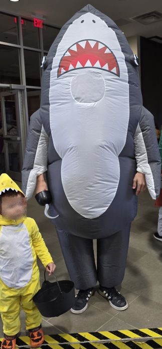 A teenager in an inflatable shark costume with an ironic hook hand next to toddler baby shark brother.